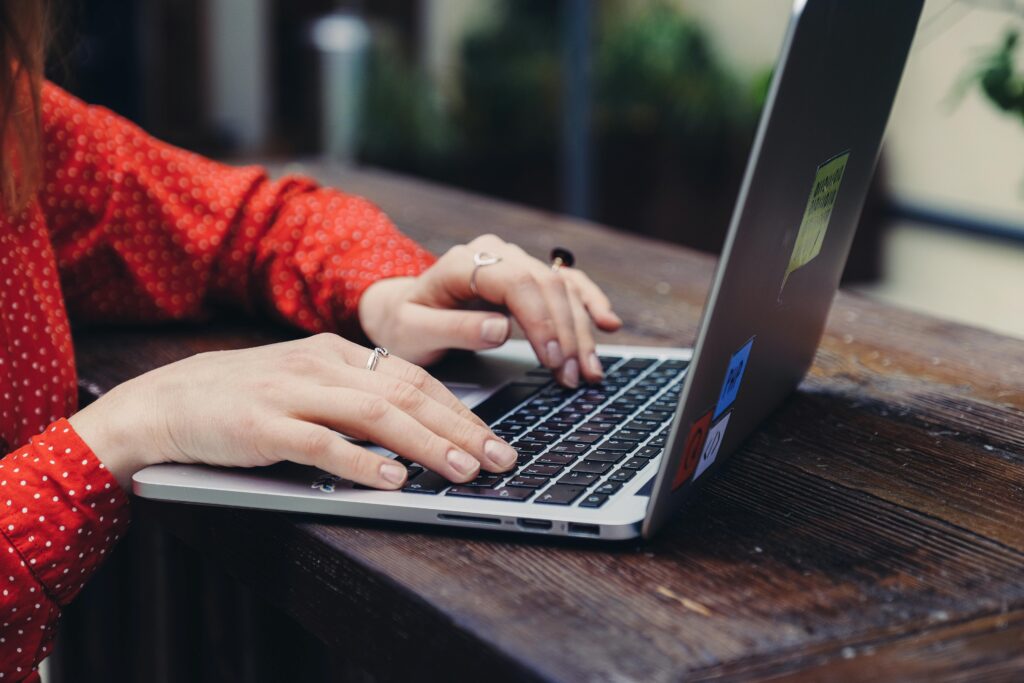 Close-up of hands typing on a laptop placed on a wooden table outdoors.